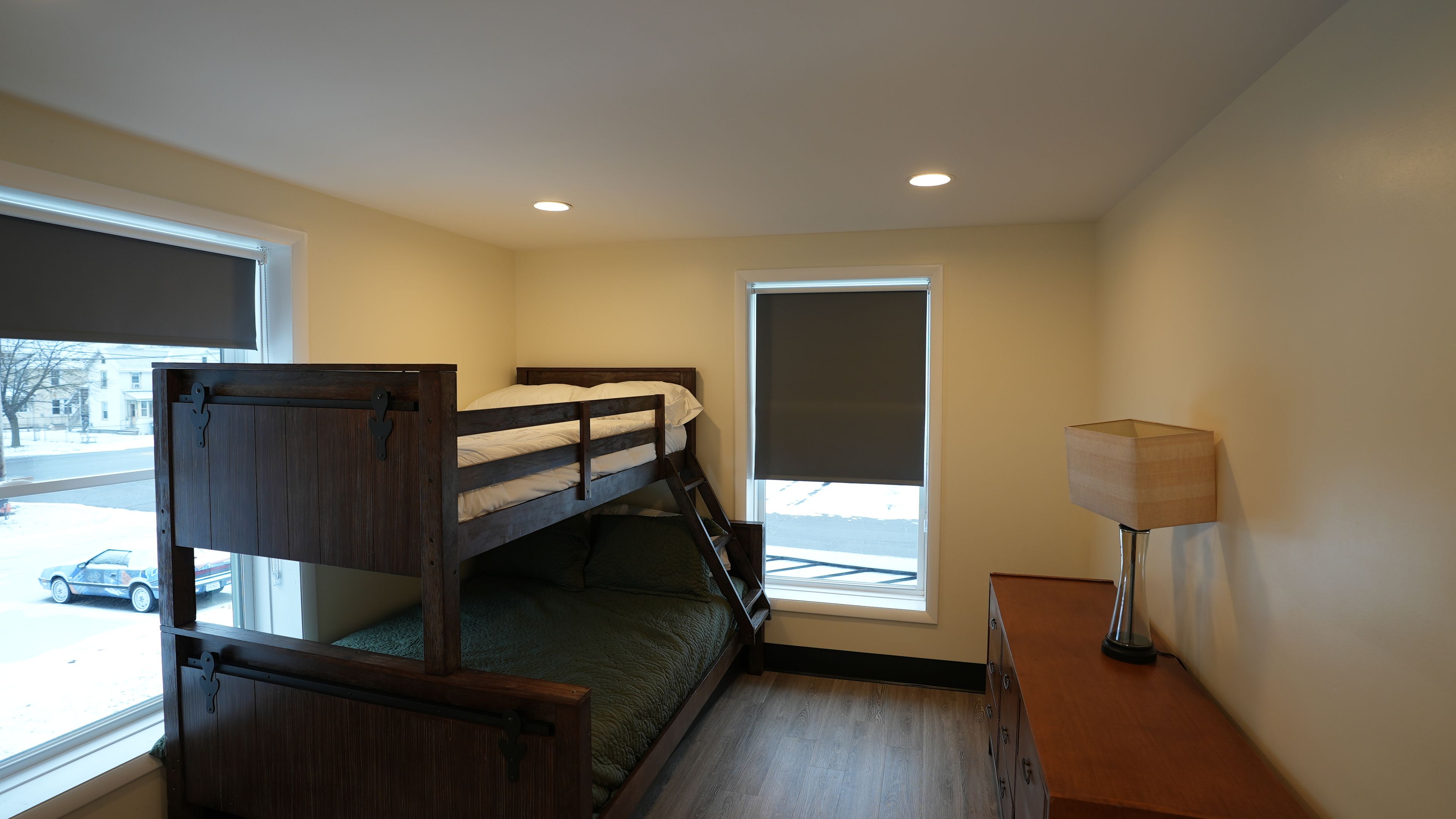 Une chambre avec un lit superposé, un bureau avec une lampe, une fenêtre donnant sur la rue et une porte.