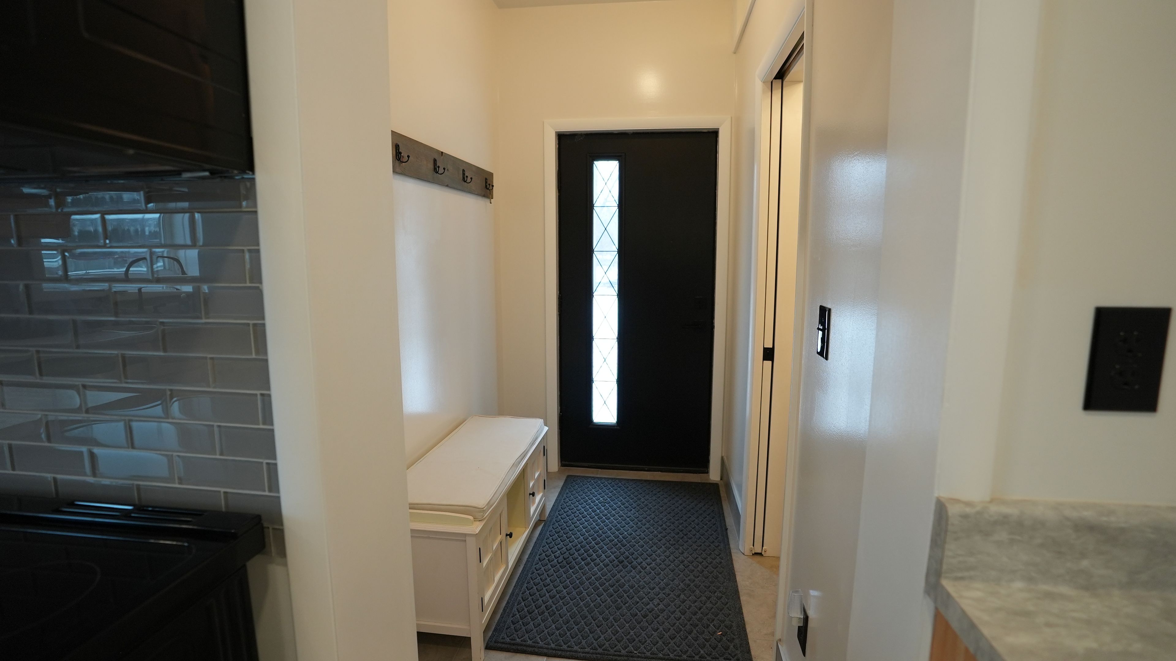 A narrow hallway with a black door, a small bench, and a tiled wall.