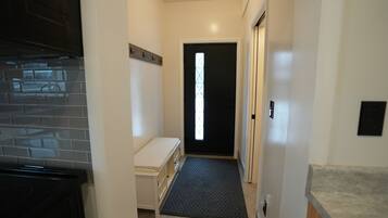 A narrow hallway with a black door, a small bench, and a tiled wall.