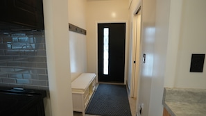 A narrow hallway with a black door, a small bench, and a tiled wall. - The Aurora House (Elmira)