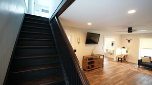 A staircase leading to a living room with a flat-screen TV, wooden flooring, and a ceiling fan.