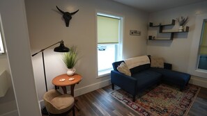 A living room with a blue sofa, a round table with a plant, a lamp, and a bull skull decoration. - The Aurora House (Elmira)