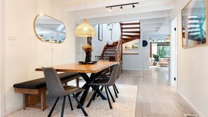 Un comedor con mesa de madera, sillas, lámpara y espejo.