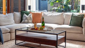 Una sala de estar moderna con una mesa de centro de vidrio, un sofá con muchos cojines y vistas al exterior.