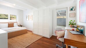 Une chambre moderne avec un lit, un bureau et un ordinateur. Les murs sont blancs, le sol est en bois et il y a une fenêtre avec des stores.
