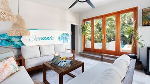 A modern living room with a sofa, coffee table, and a large window with a view of a pool and greenery. - Riverbank Blue - luxe pool, sauna, cabana and family fun moments near Minnamurra's best beaches (Minnamurra)