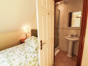 A hotel room with a bed, a nightstand, a lamp, a shower, and a sink. - Derwent Cottage (Cockermouth)