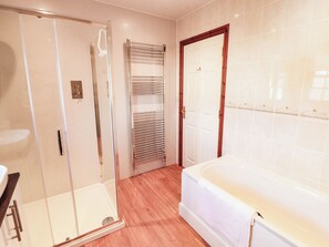 A bathroom with a glass shower enclosure, a white bathtub, and a towel rack. - Derwent Cottage (Cockermouth)