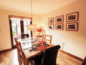 A dining area with a wooden table set for four, a red lamp, and framed pictures on the wall. - Derwent Cottage (Cockermouth)