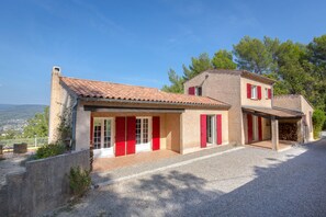 A two-story house with a red-tiled roof, a stone chimney, and a gravel driveway. - Spacious Villa Colombes with Panoramic Views, Air Conditioning, and Infinity Pool (Draguignan)