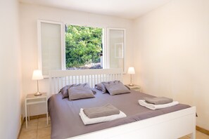 A bedroom with a bed, two bedside tables, a window with a view of greenery, and a white headboard. - Spacious Villa Colombes with Panoramic Views, Air Conditioning, and Infinity Pool (Draguignan)