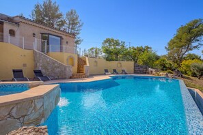 A swimming pool with a stone wall and a building with a balcony. - Spacious Villa Colombes with Panoramic Views, Air Conditioning, and Infinity Pool (Draguignan)
