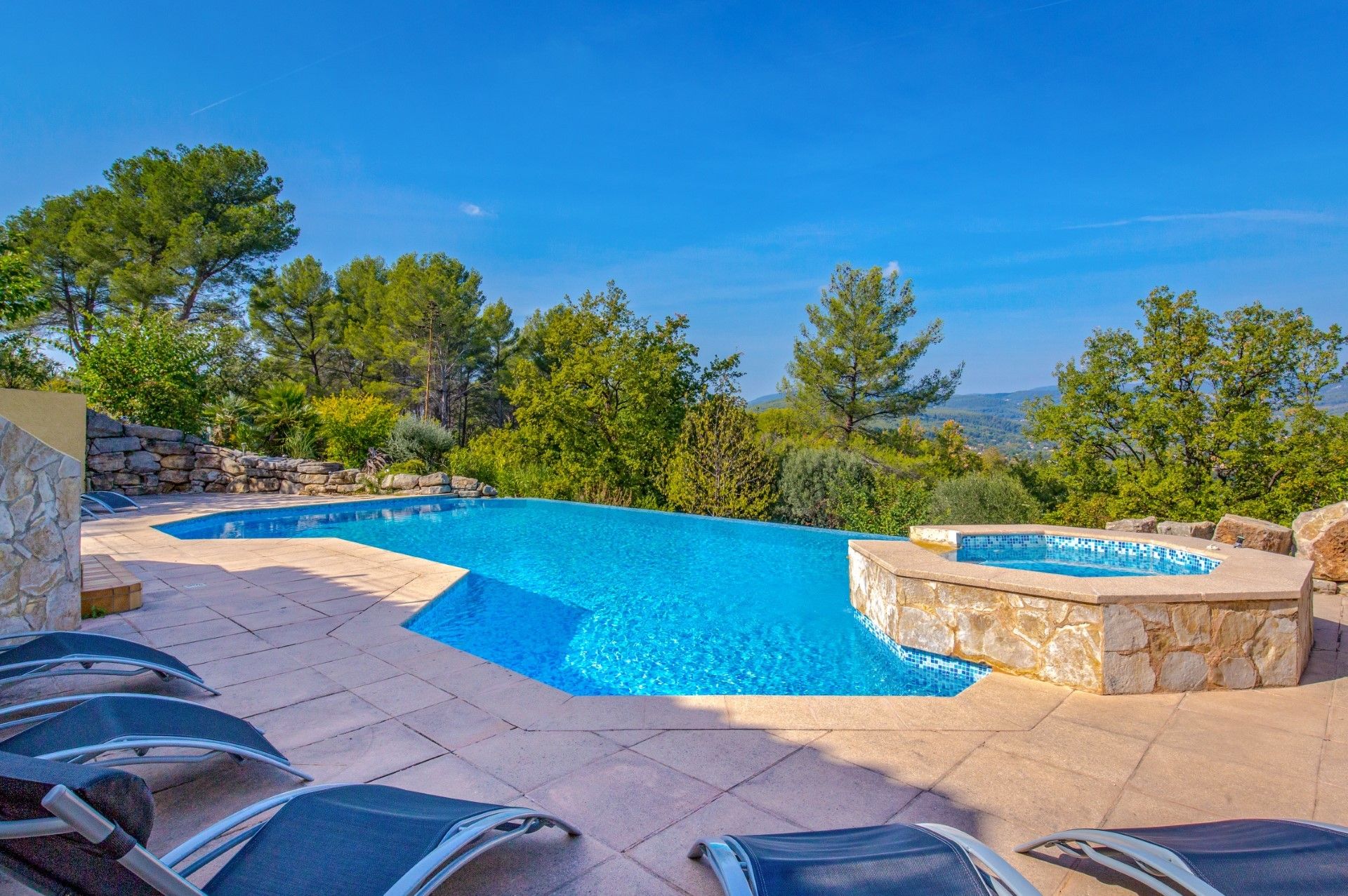 A swimming pool with a stone border, surrounded by lounge chairs and a stone wall.