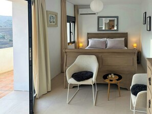 Una camera da letto con un letto, due sedie, un comodino con candele, una finestra con tende e vista sull'esterno.
