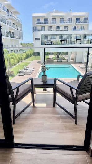 A balcony with a pool view, outdoor furniture, and a modern building in the background. - Earthing Central Park Suiteconnect and Rest (Punta Cana)