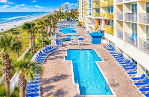 Ein Poolbereich eines Resorts mit mehreren Schwimmbecken, Liegestühlen und Blick auf den Strand.