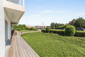 A residential property with a paved deck, manicured lawn, and a row of houses in the background. - Delvaux B 001 met garage (NIEUWPOORT)