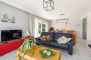 A modern living room with a flat-screen TV, a leather sofa, a coffee table with decorative items, and a dining area with wicker furniture. - Delvaux B 001 met garage (NIEUWPOORT)