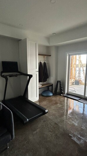 A room with a treadmill, a bench, and a door leading to a balcony with a view.