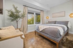 A bedroom with a bed, a chair, a window, and a plant.