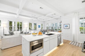 Une cuisine moderne avec des meubles blancs, un îlot central et un coin repas comprenant un canapé et des chaises.