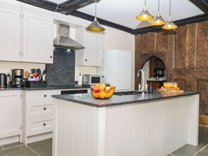 A modern kitchen with white cabinetry, a black countertop, and a central island with fruit. - The Abbey Grange (Bridport)