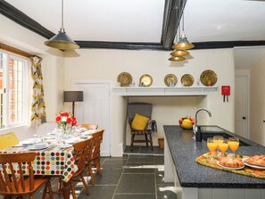 A kitchen with a dining table set for four, a breakfast bar with croissants and orange juice, and a window with curtains. - The Abbey Grange (Bridport)