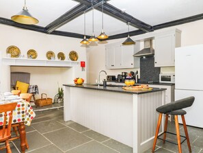 A modern kitchen with a central island, white cabinetry, and a dining area with a polka-dotted tablecloth. - The Abbey Grange (Bridport)