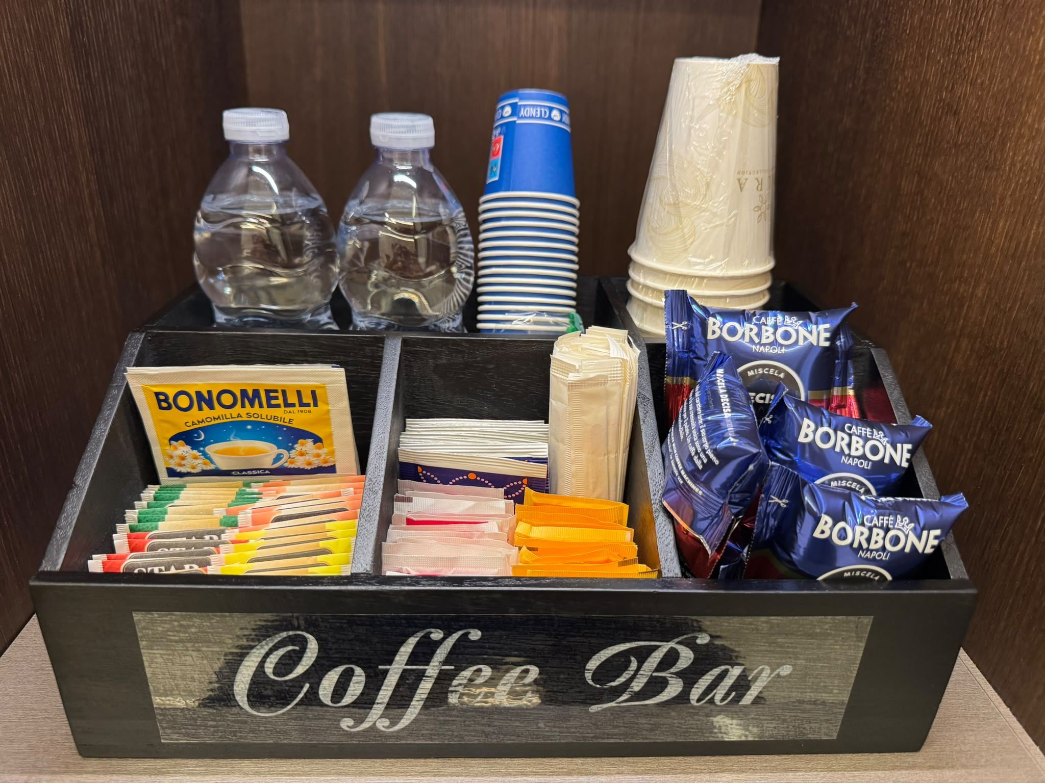 En kaffebar med olika tillbehör, inklusive Bonomelli-kaffe, Borbone Napoli-snacks och staplade tallrikar.
