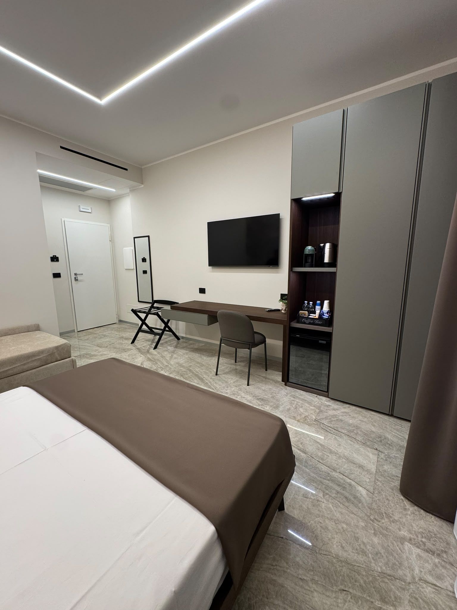 Ein Hotelzimmer mit einem Bett, einem Schreibtisch, einem Sessel, einem Fernseher und einer Kaffeebar.
