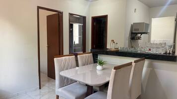Un comedor con una mesa y sillas blancas, una planta en maceta y una cocina con armarios y microondas.