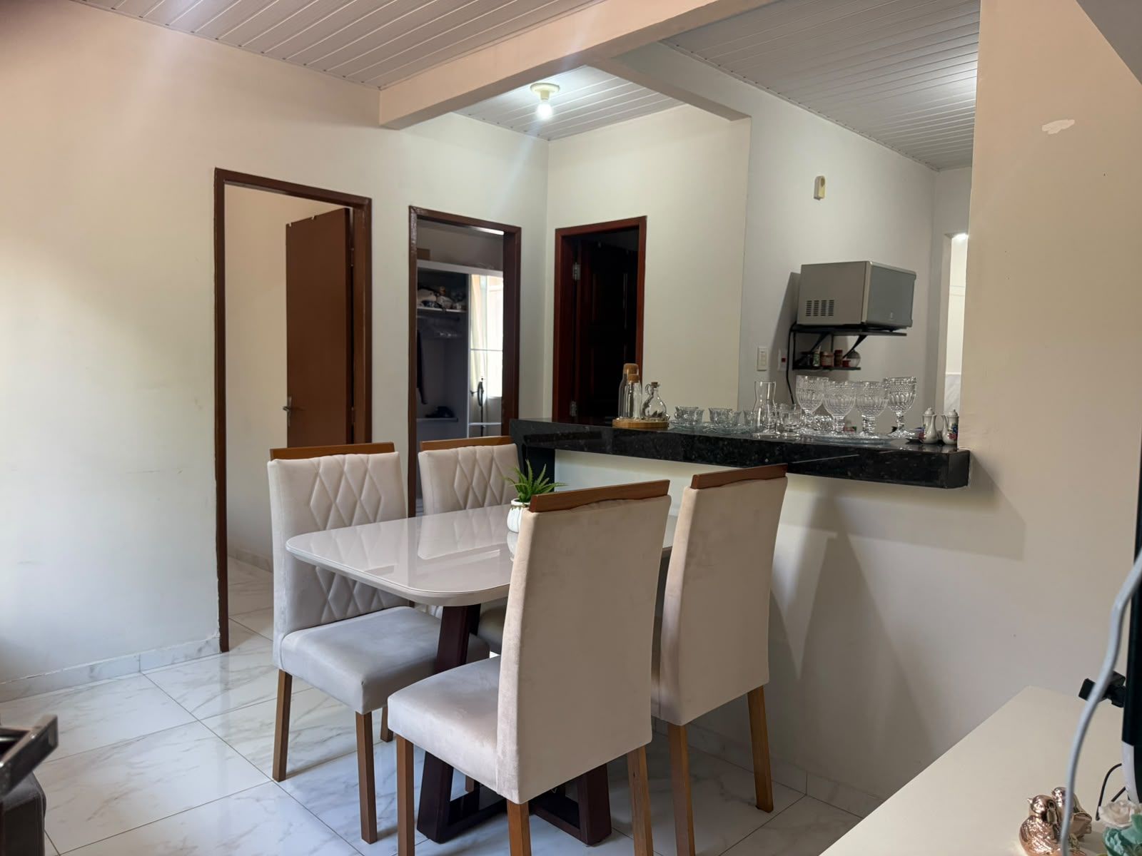 A dining area with a white table and chairs, a kitchen with a black countertop, and a white tiled floor.