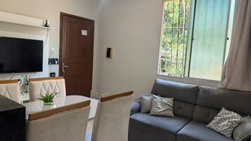 A living room with a sofa, a television, and a dining area with chairs.
