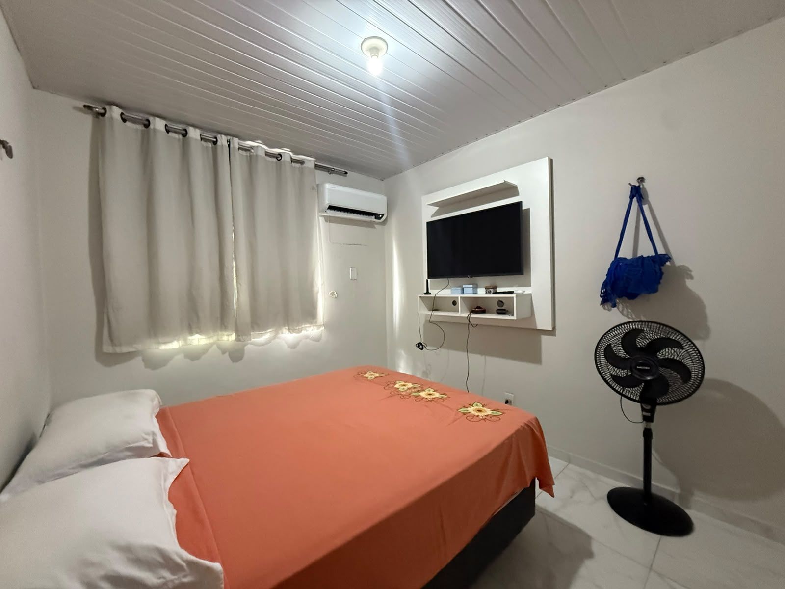 Une chambre avec un lit, un appareil de climatisation, une télévision et un ventilateur sur pied.