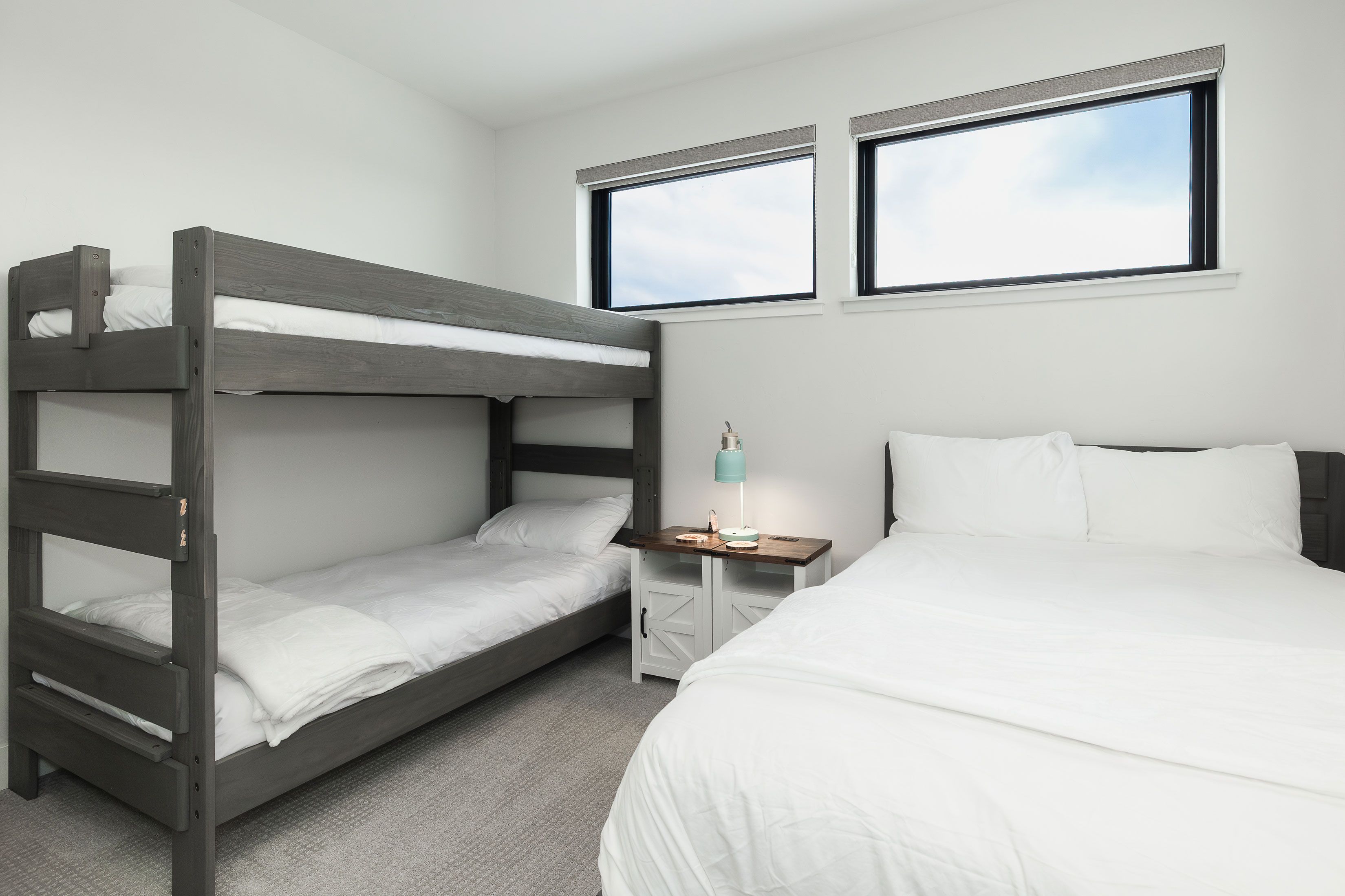 A bunk bed with white bedding, a bedside table with a lamp, and a single bed with white bedding.