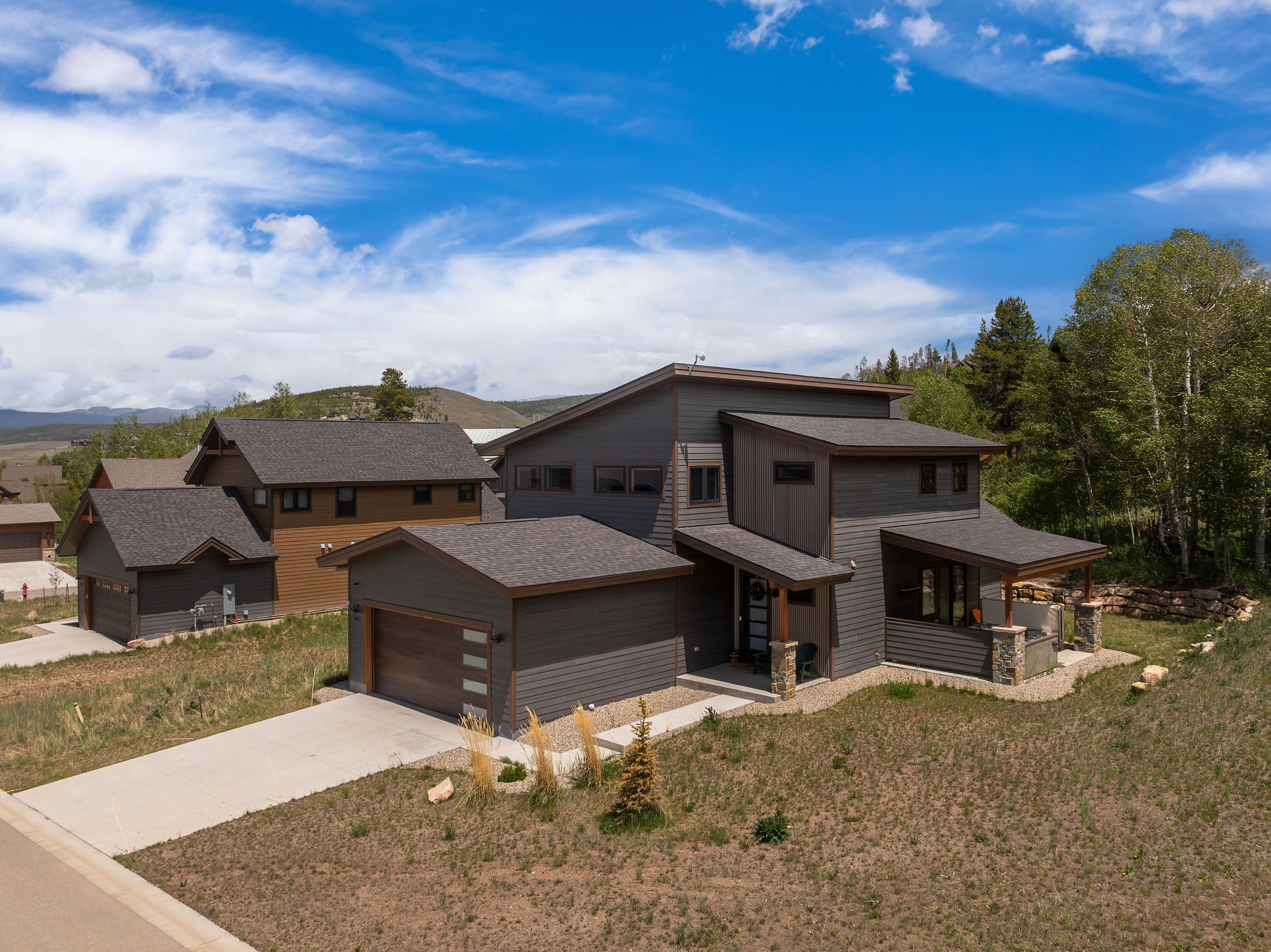 A modern multi-story house with a garage, a covered outdoor seating area, and a view of the surrounding landscape.
