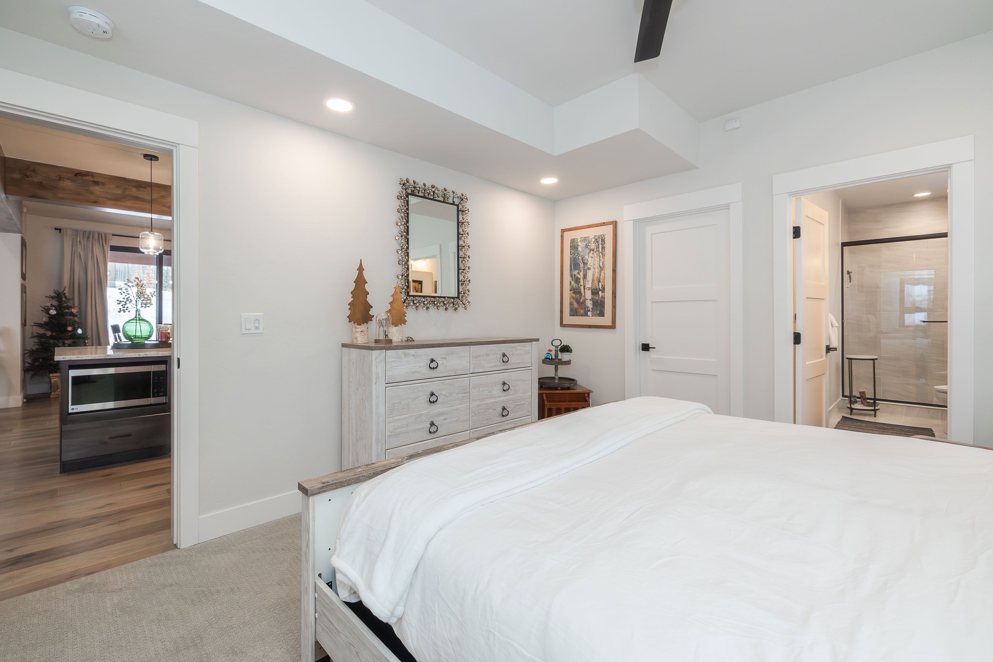 A bedroom with a large bed, a dresser, a mirror, and a door leading to a bathroom.