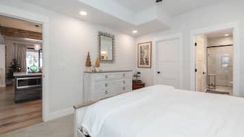 A bedroom with a large bed, a dresser, a mirror, and a door leading to a bathroom.