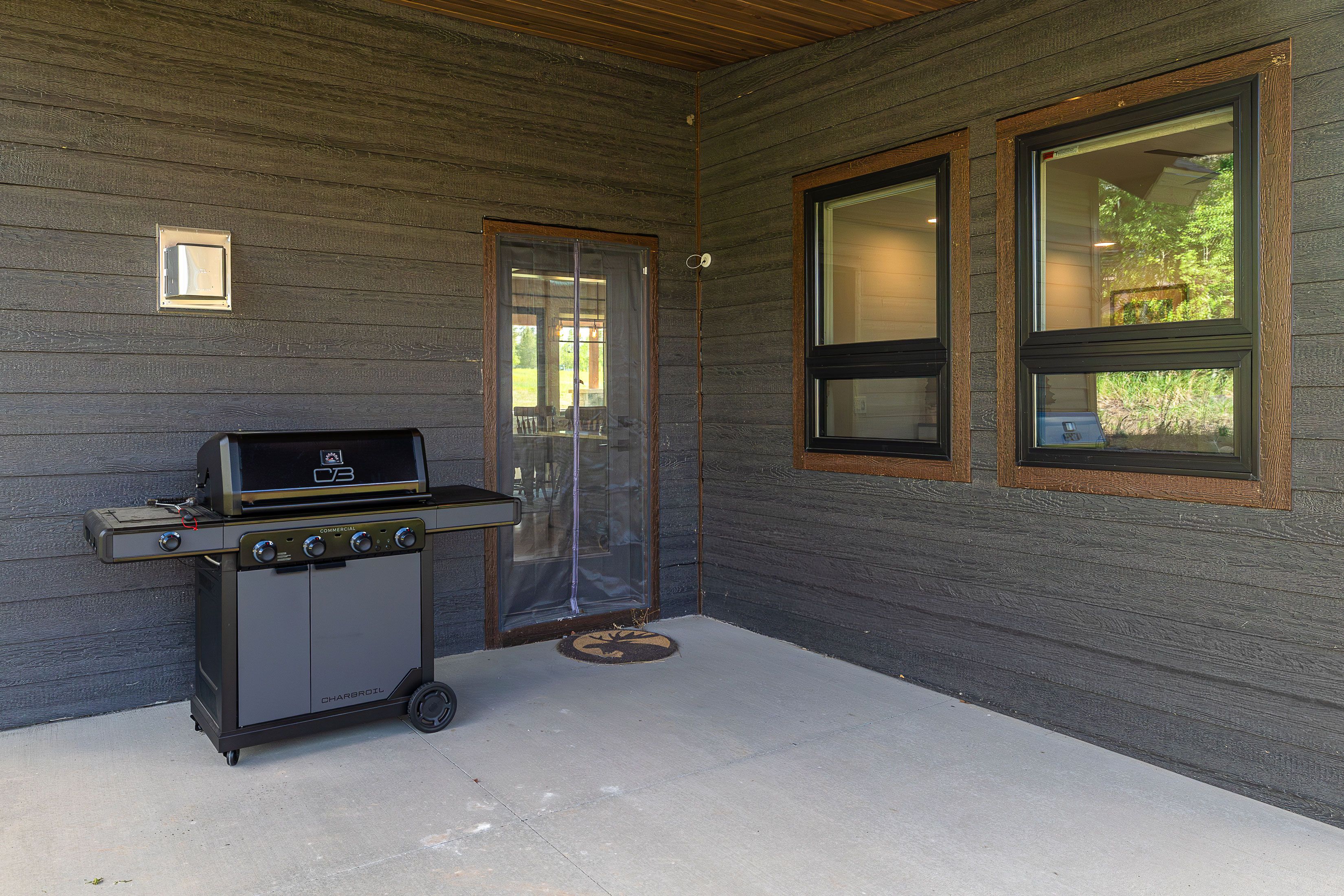 An outdoor patio with a commercial grill, a sliding glass door, and two windows with blinds.