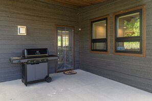 An outdoor patio with a commercial grill, a sliding glass door, and two windows with blinds.