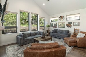 A spacious living room with a large window, a gray sofa, a brown leather chair, and a coffee table.