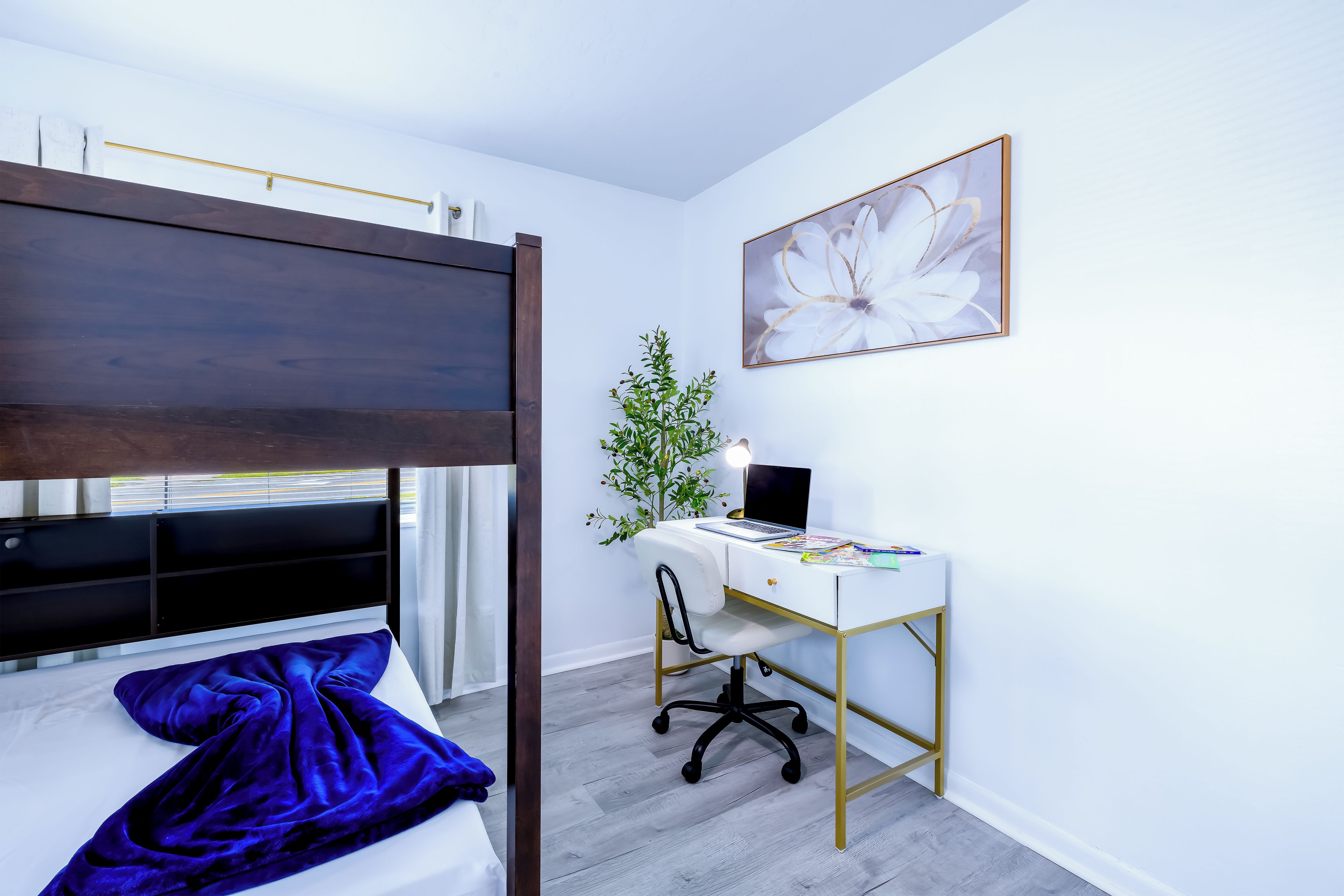 Un dormitorio con una cama litera, un escritorio con computadora y un cuadro grande de flores en la pared.