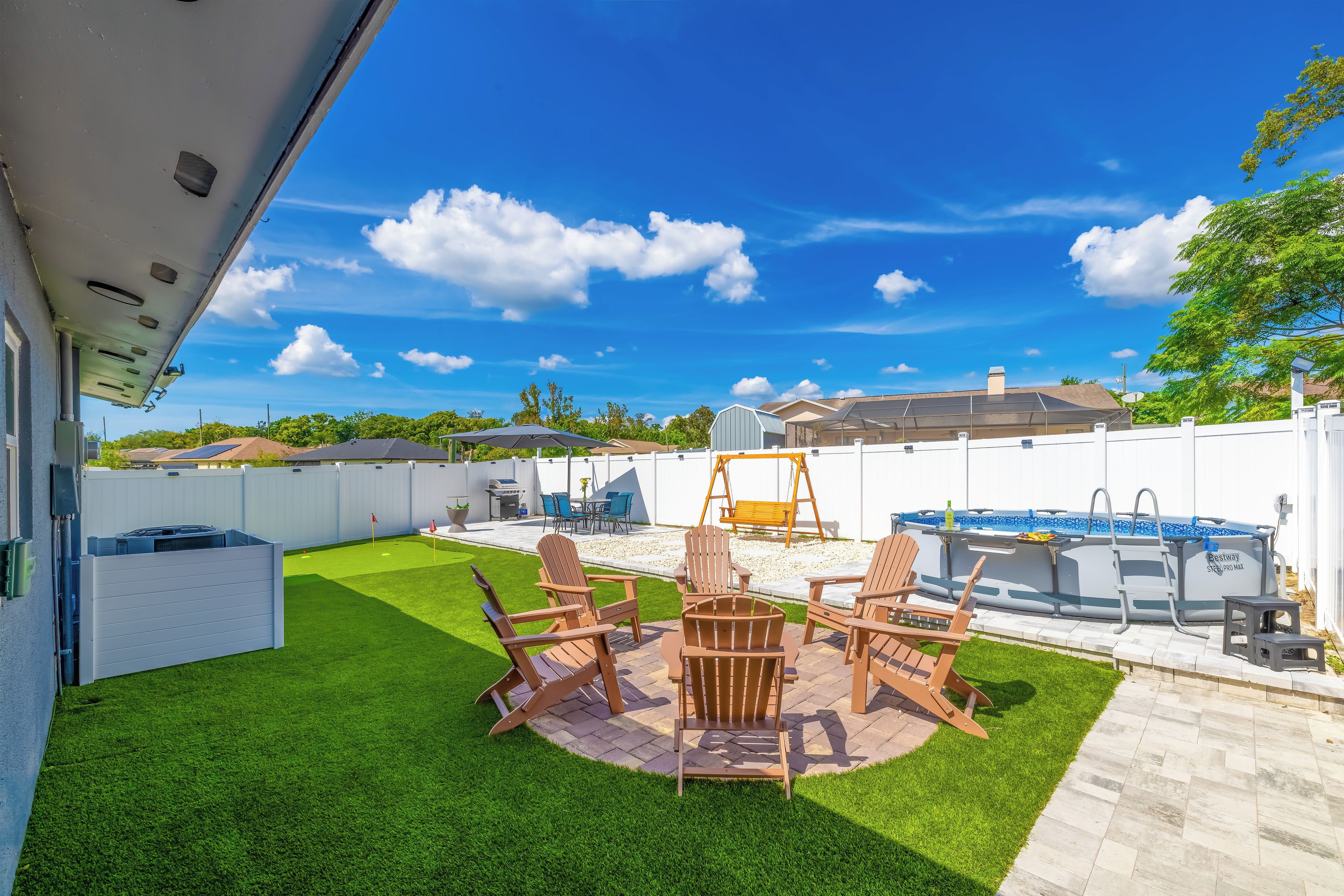 A backyard with artificial grass, a patio with outdoor furniture, a swing set, and a swimming pool.