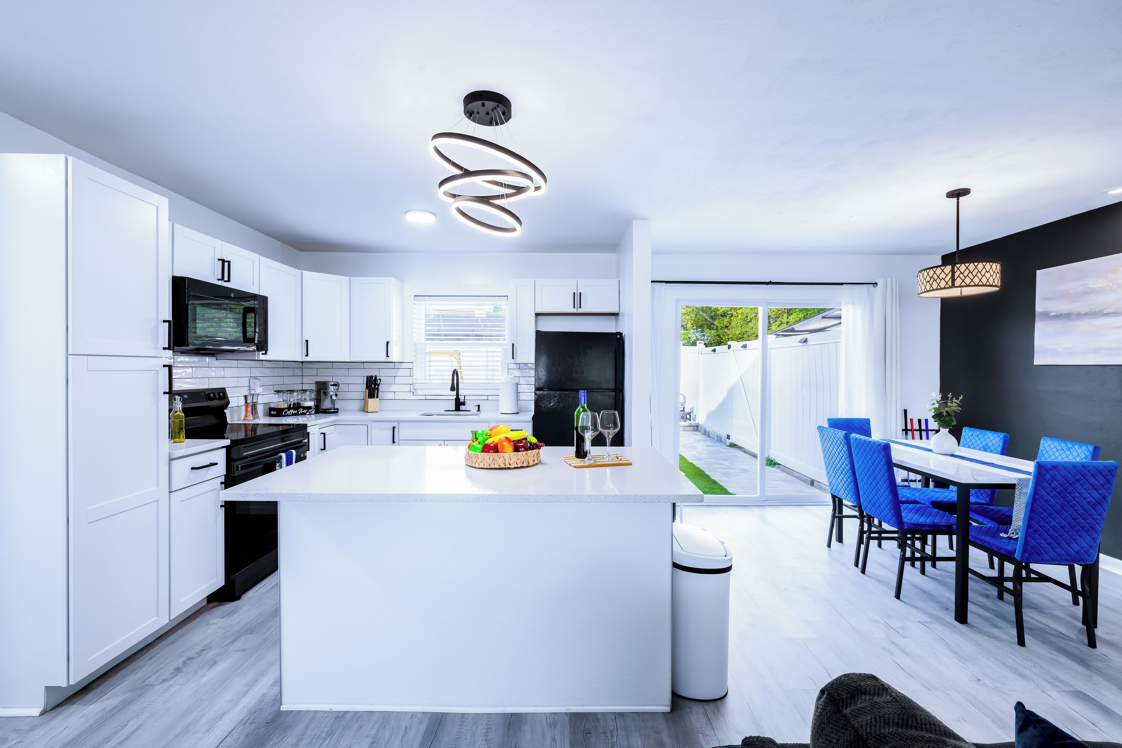 Una cocina moderna con armarios blancos, una isla central y un comedor con sillas azules.