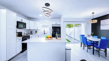 Una cocina moderna con armarios blancos, una isla central y un comedor con sillas azules.