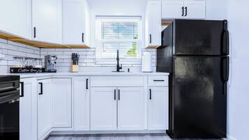 A modern kitchen with white cabinets, a black refrigerator, and a coffee machine.