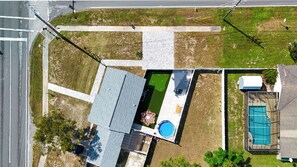 Vista aérea de una propiedad residencial con piscina, un patio amueblado y un jardín cercado.