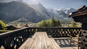 A wooden deck with a railing overlooking a mountainous landscape with snow-capped peaks and a village below. - Chalet La Renarde-a rare and unique 5-bedroom chalet near the centre of Chamonix (Chamonix-Mont-Blanc)
