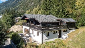 Eine zweistöckige Chalet mit Balkon, eingebettet in eine Berglandschaft mit dichtem Wald.