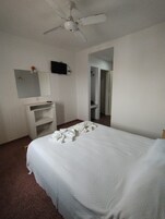 Una habitación de hotel con cama, escritorio con espejo, televisión y ventilador de techo.